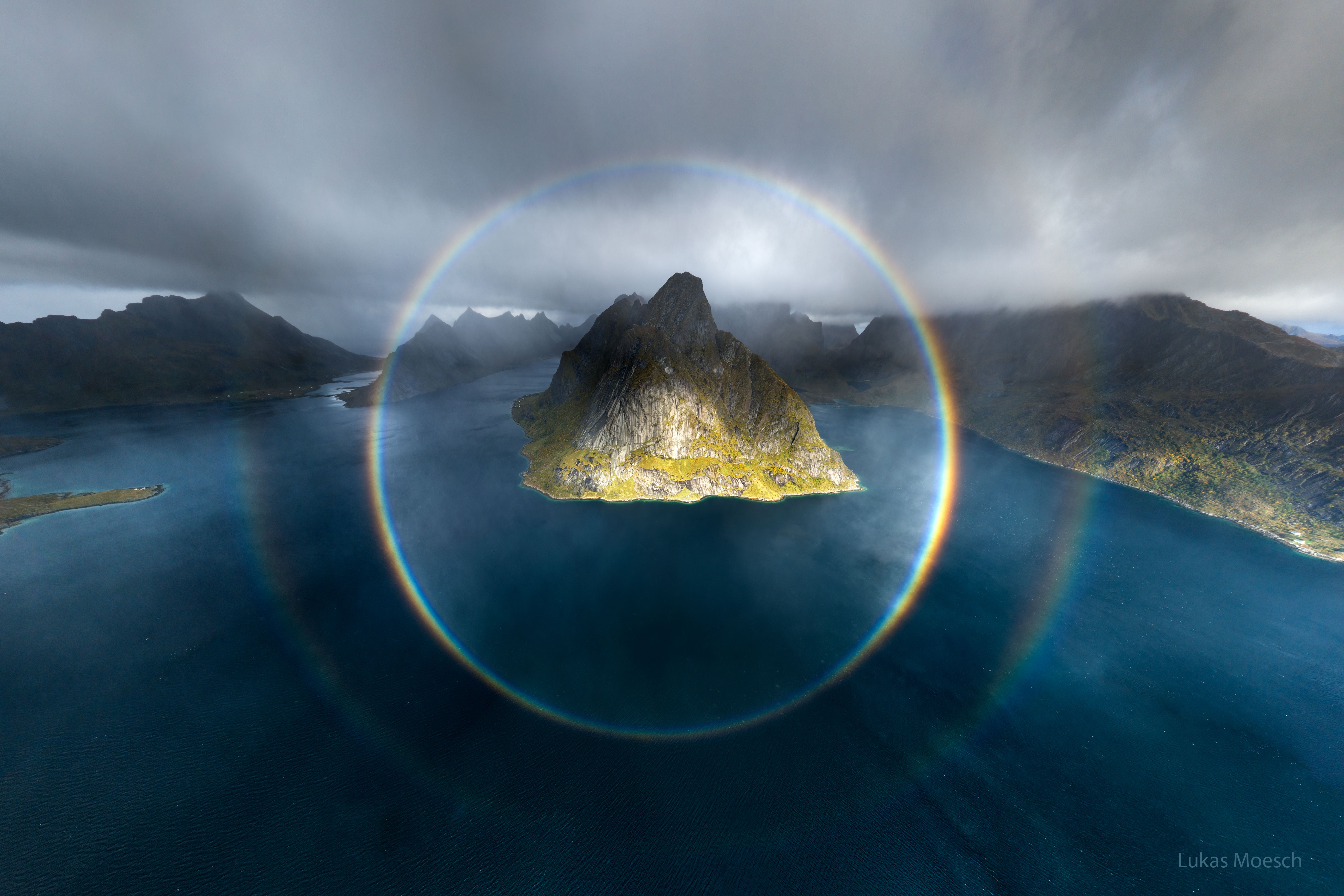 The featured image shows two complete circular rainbows centered on a mountainous island. Please see the explanation for more detailed information.
