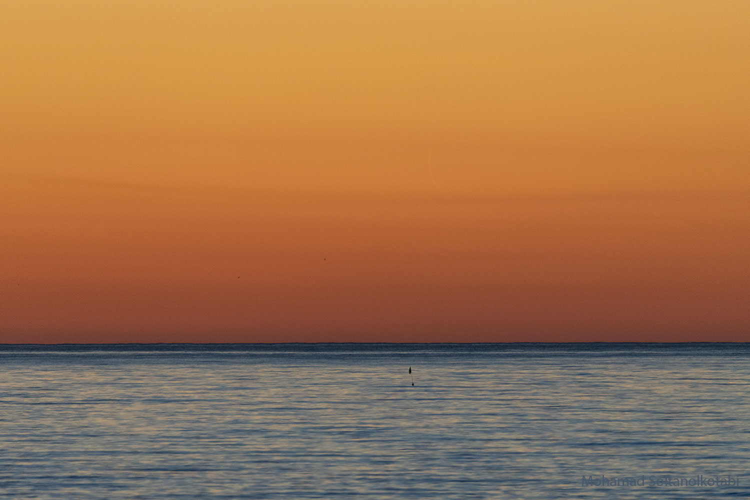 The featured image shows an orange sky over water with a very faint, slight crescent Moon in the sky. Please see the explanation for more detailed information.