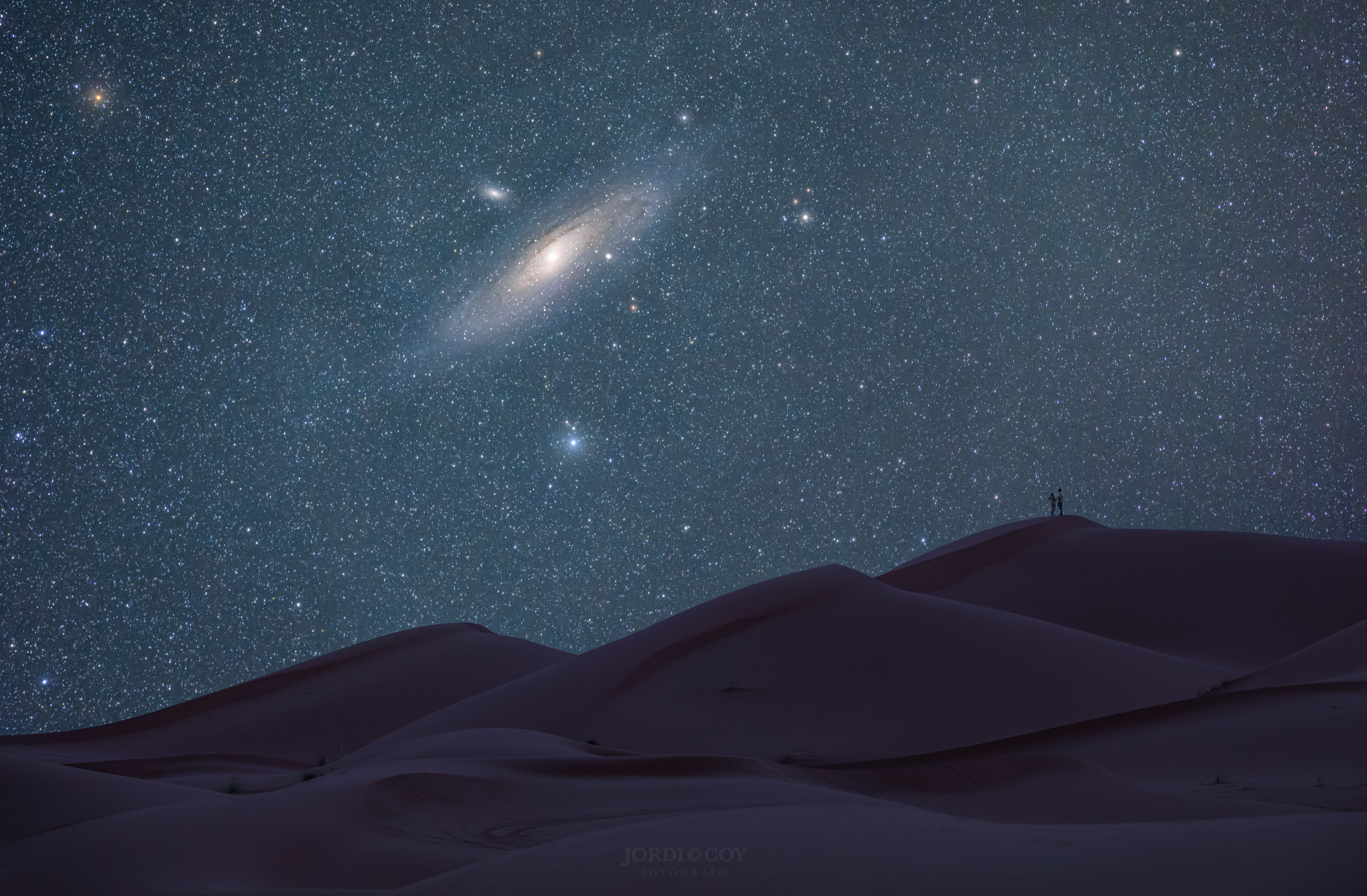 The featured image shows a zoom into the Andromeda Galaxy over dunes in the Sahara Desert. Two people are barely visible at the top of one of the dunes. Please see the explanation for more detailed information.