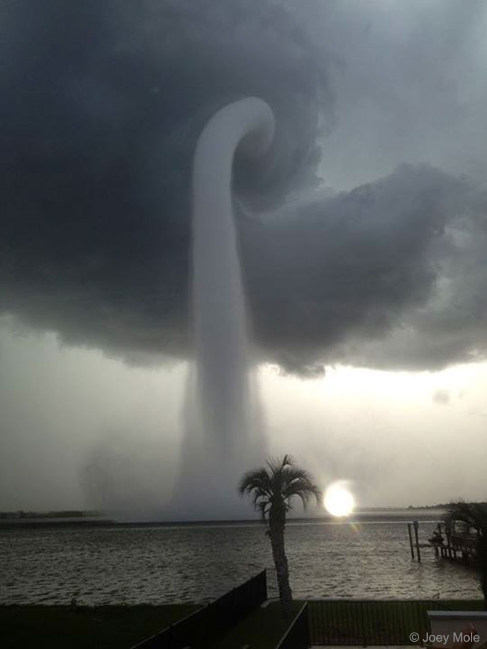 A thin gray funnel cloud is pictured connecting water at the bottom to a cloud near the top. Please see the explanation for more detailed information.