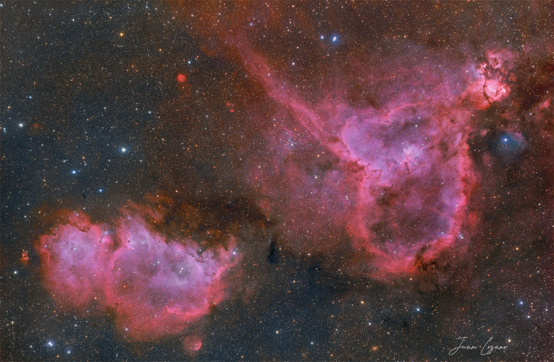 Two red emission nebulas are shown in front of a dark but colorful starfield. The Soul Nebula is on the lower left, while the Heart Nebula is on the upper right. Please see the explanation for more detailed information.