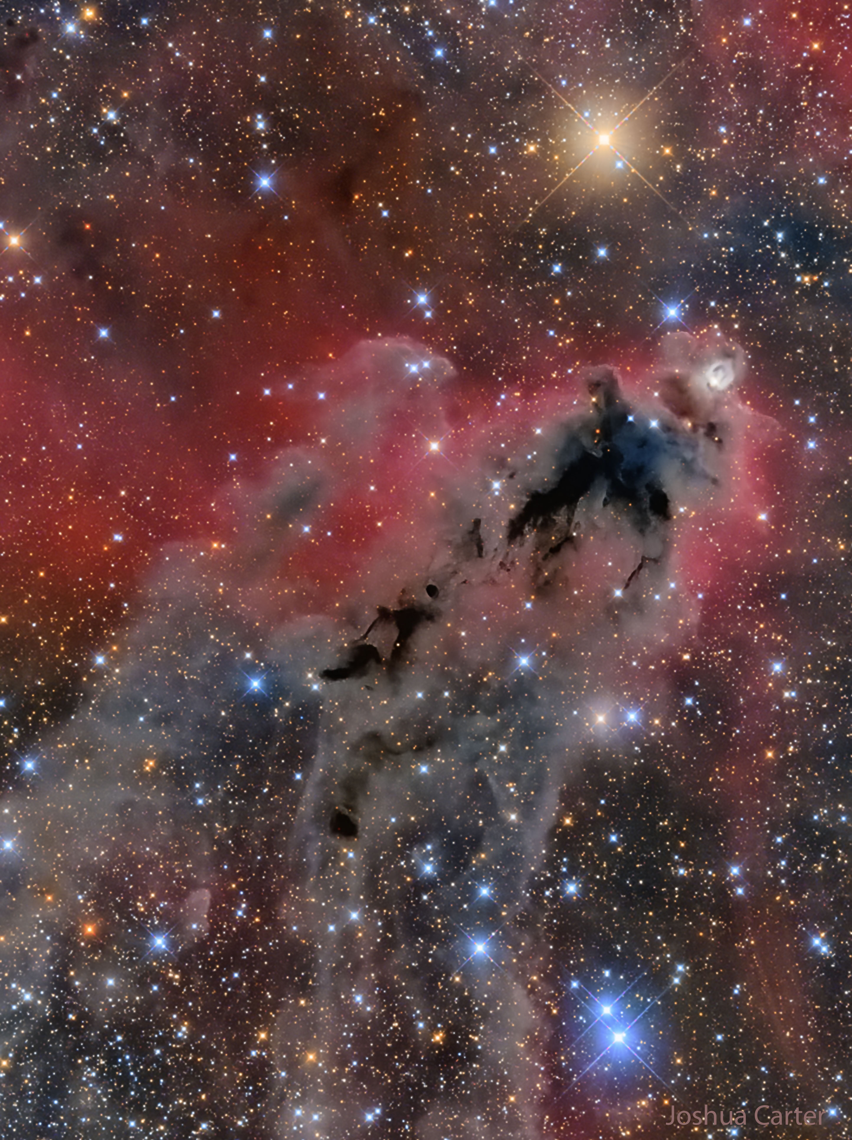 An image of a foreboding dark nebula before a red-glowing gas background and many bright and colorful stars. Please see the explanation for more detailed information.