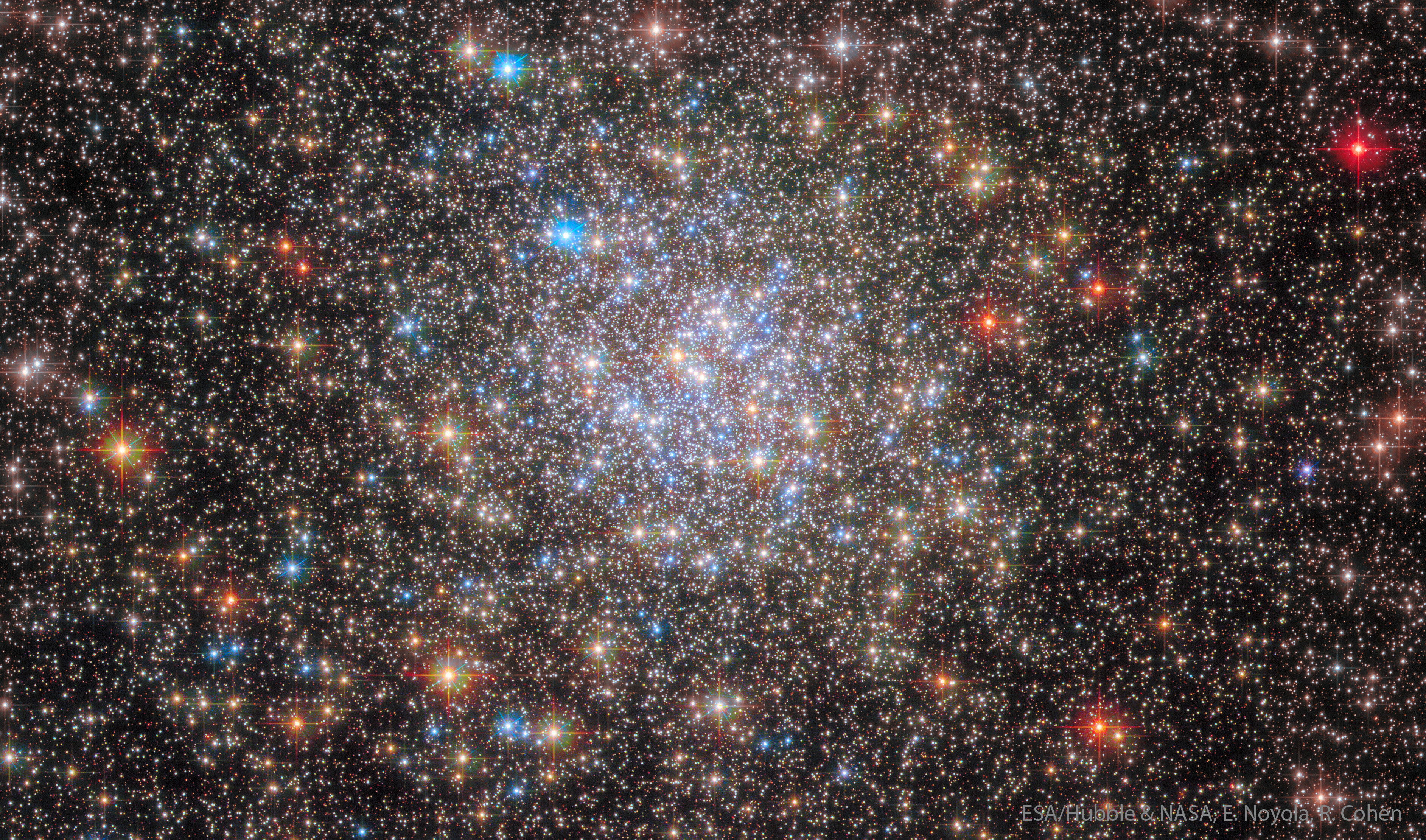 A ball of stars containing thousands of stars is shown with mostly light colored stars but with some stars having vibrant colors. Please see the explanation for more detailed information.