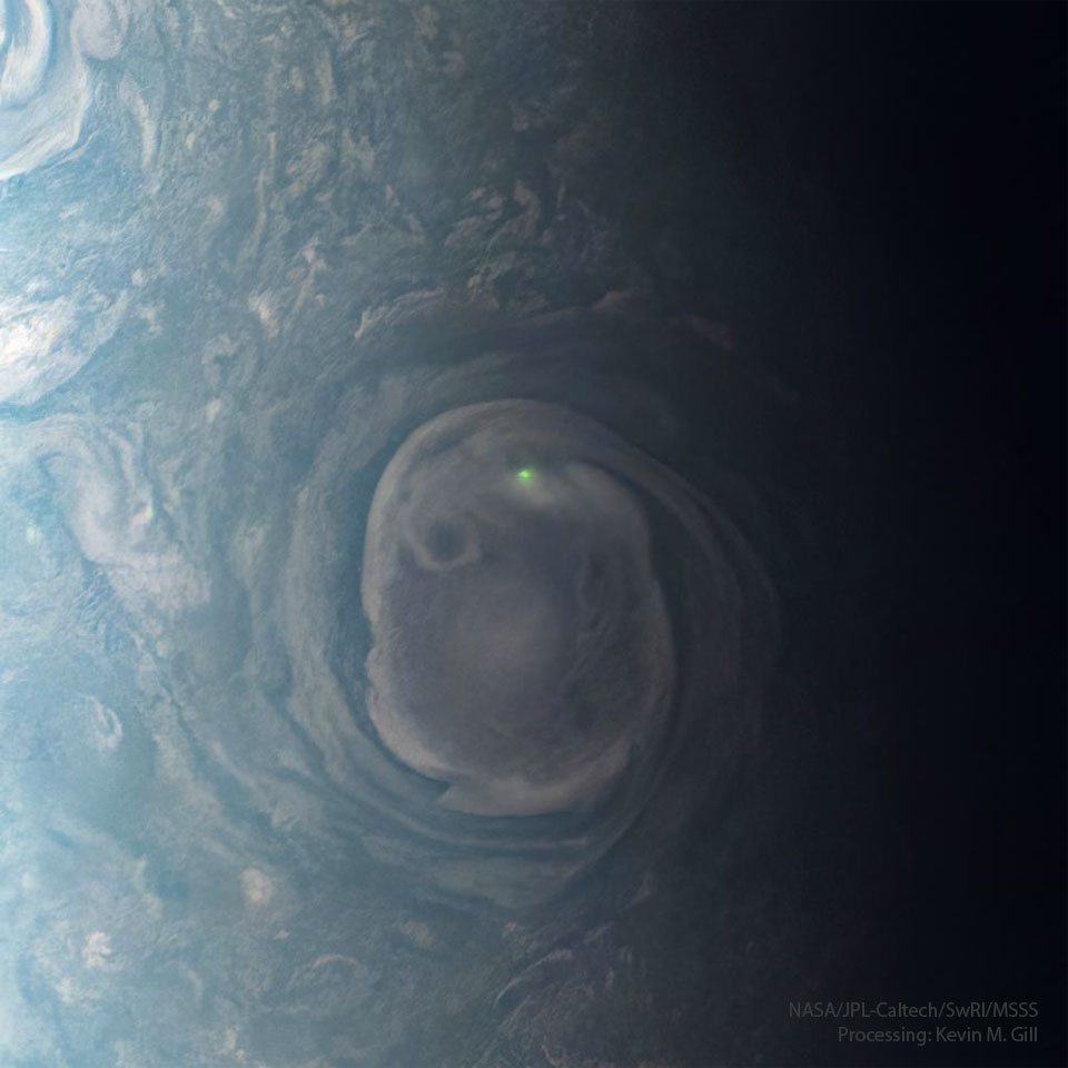A large swirling cloud on Jupiter is shown with a bright green spot near its top. The cloud is surrounded by other less descript parts of Jupiter's upper atmosphere. Please see the explanation for more detailed information.