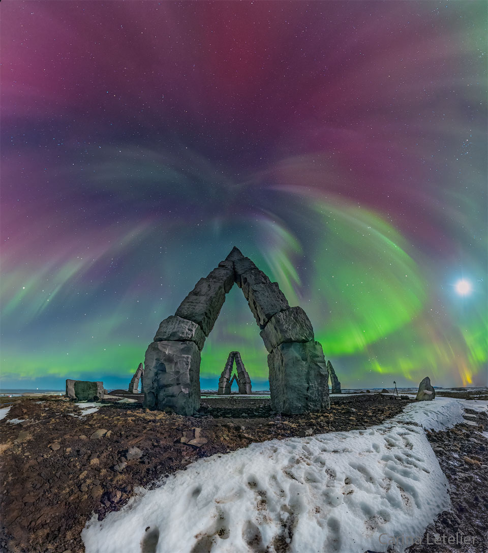 Multi-colored aurora are seen above an unusual stone gateway, the first of several similar gateways seen in the distance. Please see the explanation for more detailed information.