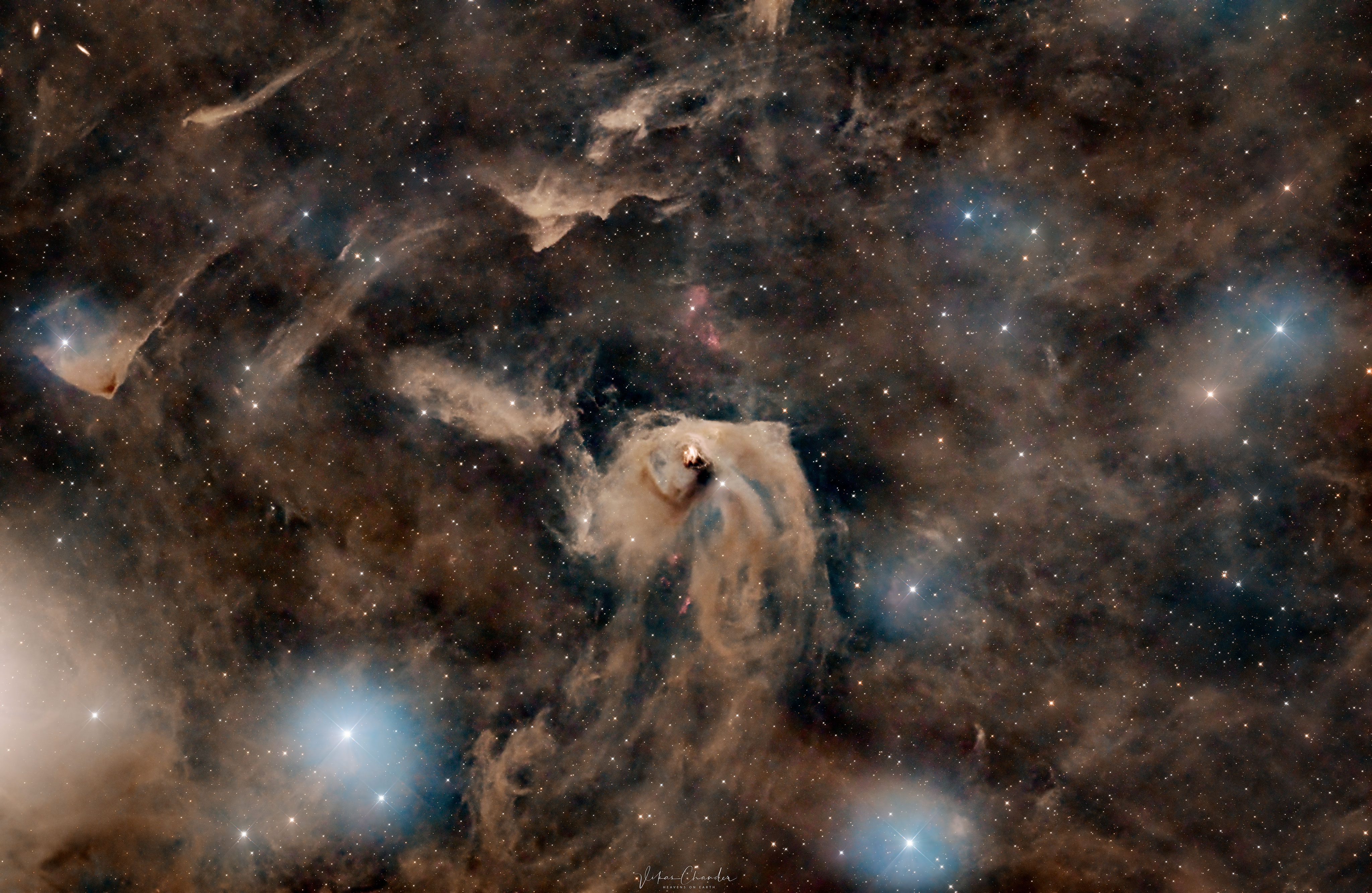 A star field strewn with bunches of brown dust is pictured. In the center is a bright area of light brown dust, and in the center of that is a bright region of star formation. Please see the explanation for more detailed information.