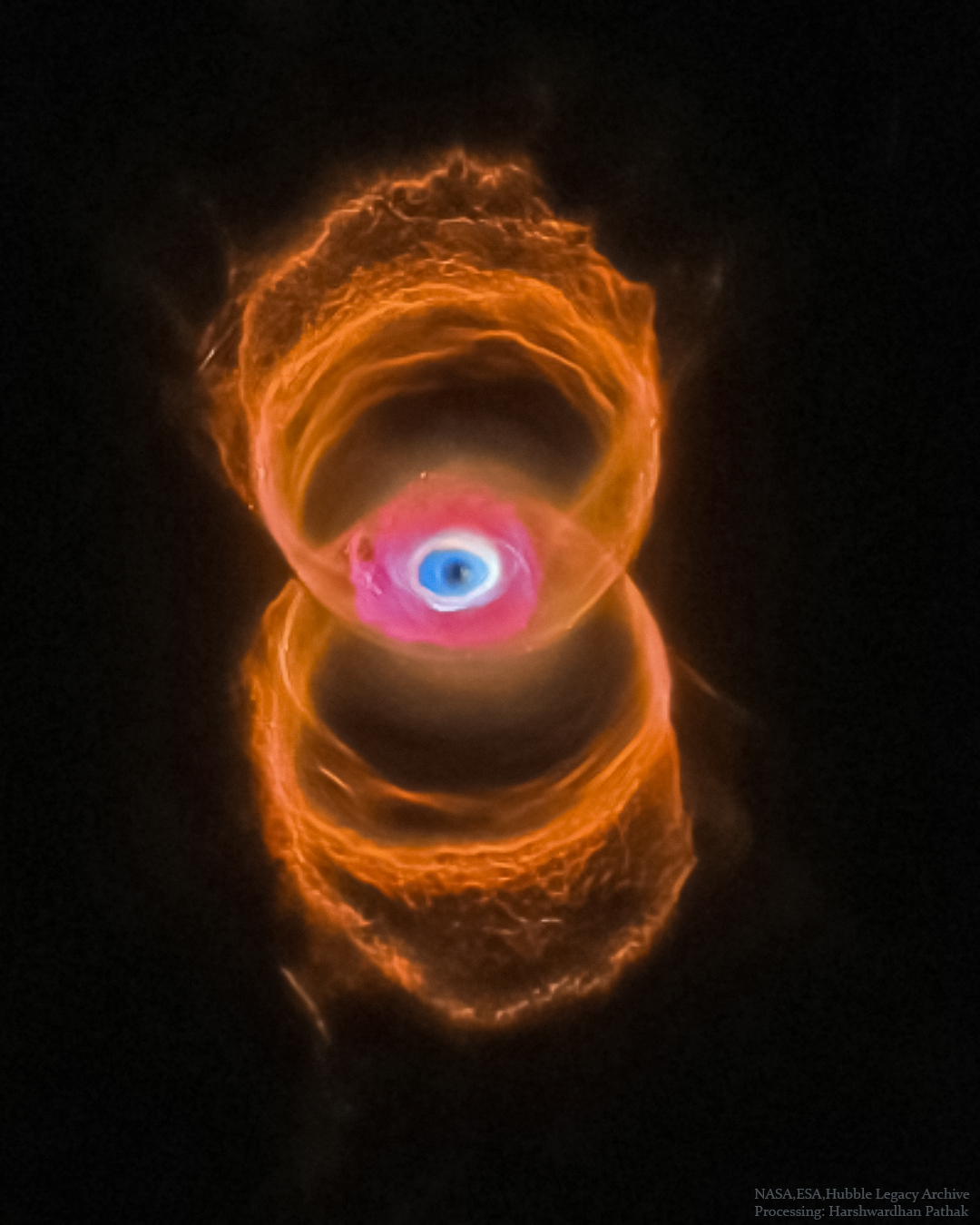 A vertical planetary nebula is shown in orange around the outside but with a blue glow in the center. The outside is shaped like a tilted hourglass, while the inside appears similar to an eye. Please see the explanation for more detailed information.
