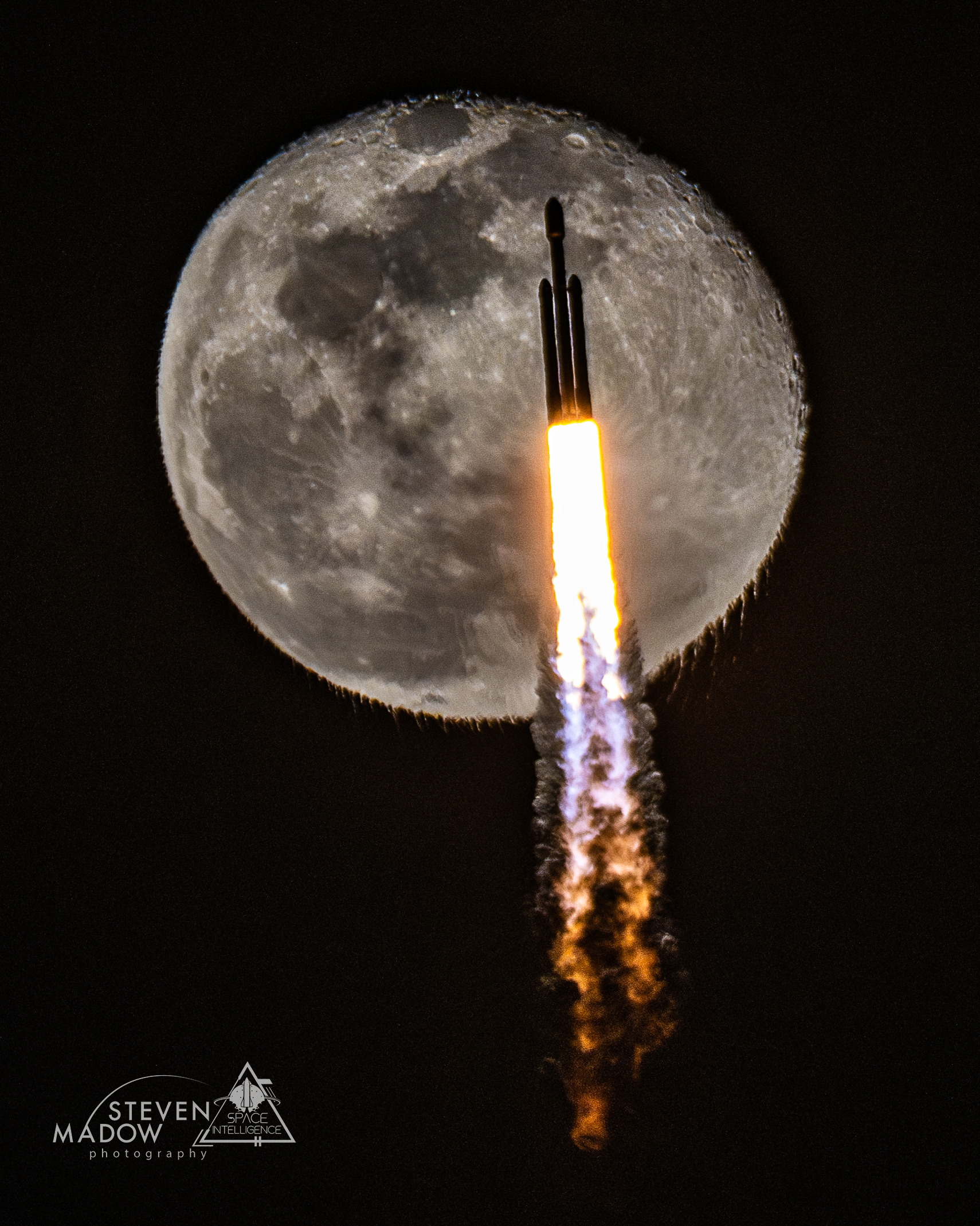A rocket is pictured ascending during launch. A nearly full moon is behind it. The rocket exhaust, itself visible, causes the bottom of the Moon to appear unusually rippled. Please see the explanation for more detailed information.
