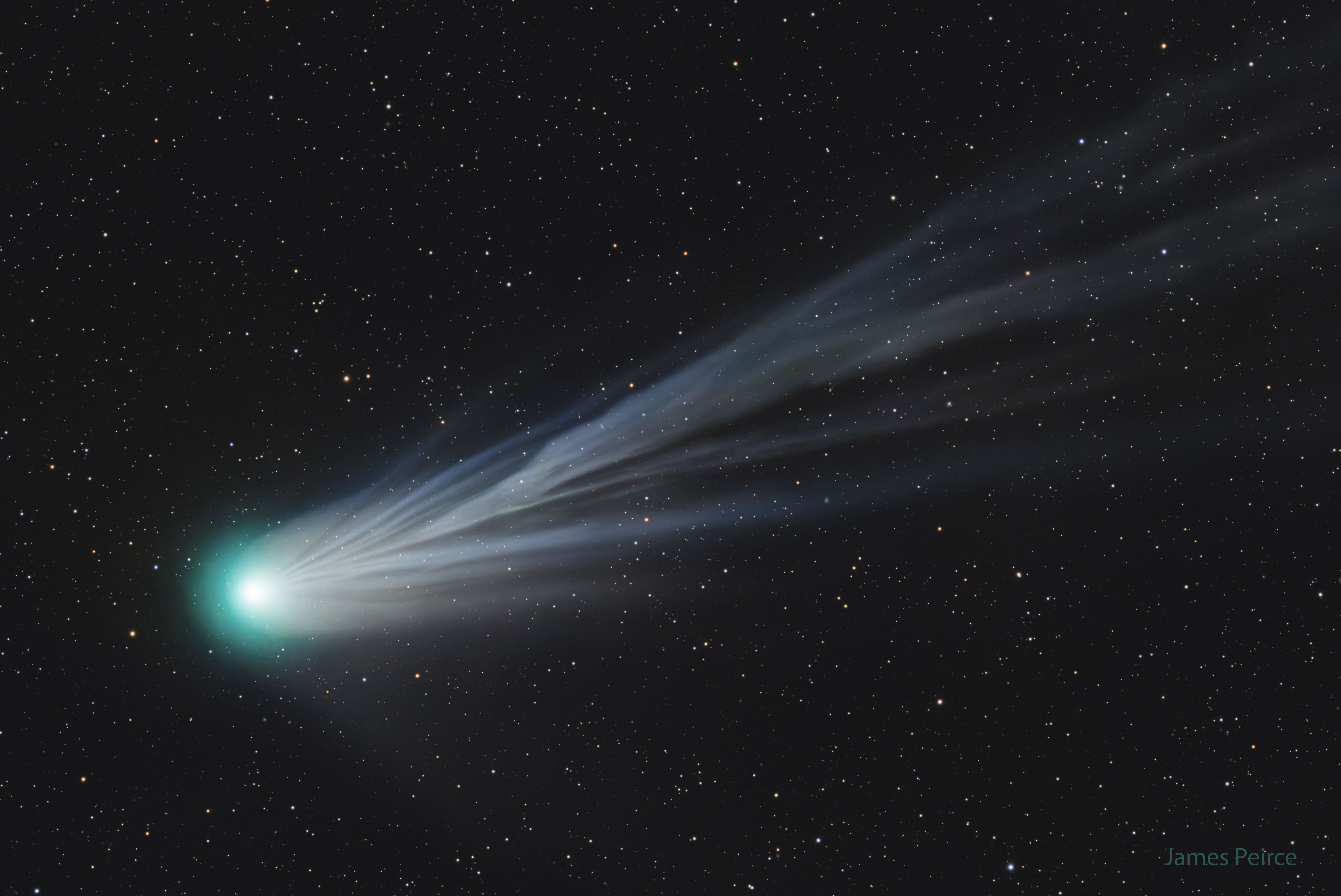 A large comet is shown with its head near the right and a light blue flowing ion tail flowing across into the rest of the image. Please see the explanation for more detailed information.