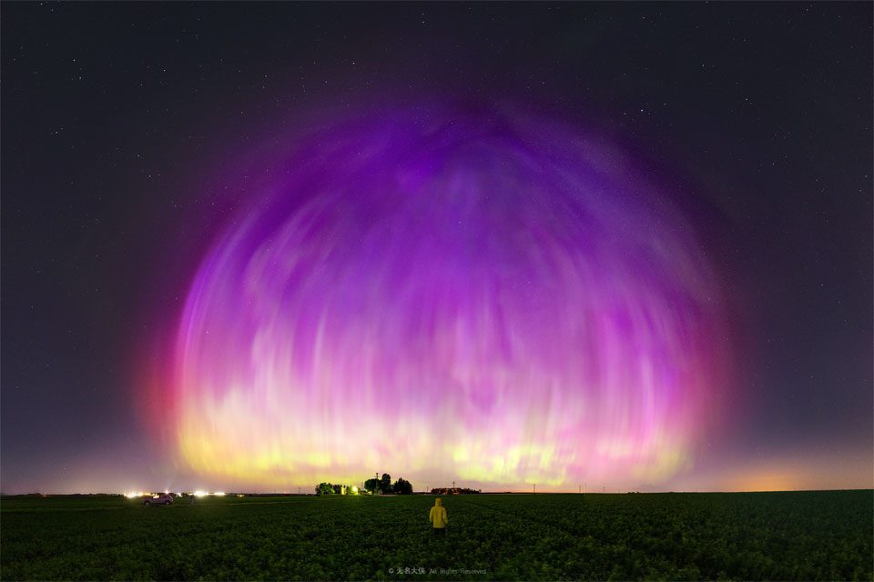 A large purple transparent dome appears to cover much of a starry sky. A person stands in a field looking toward the unusual spectacle. Please see the explanation for more detailed information.