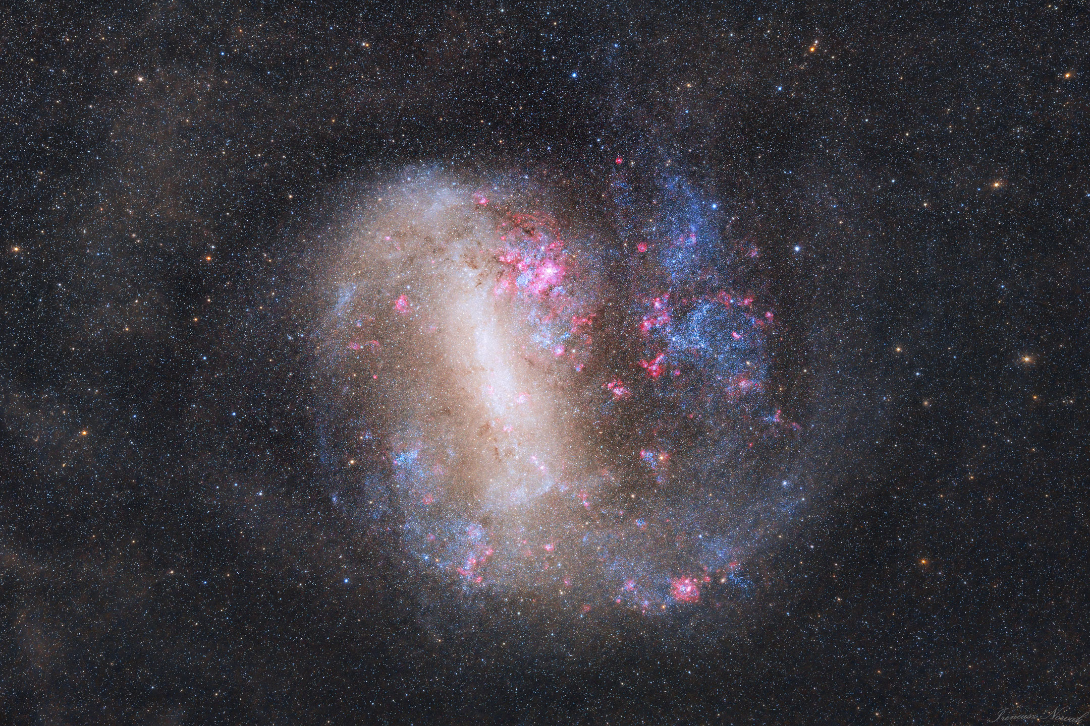 An unusual looking galaxy is shown with a light bar running nearly vertical and blue stars and red nebulas around the edges. Please see the explanation for more detailed information.