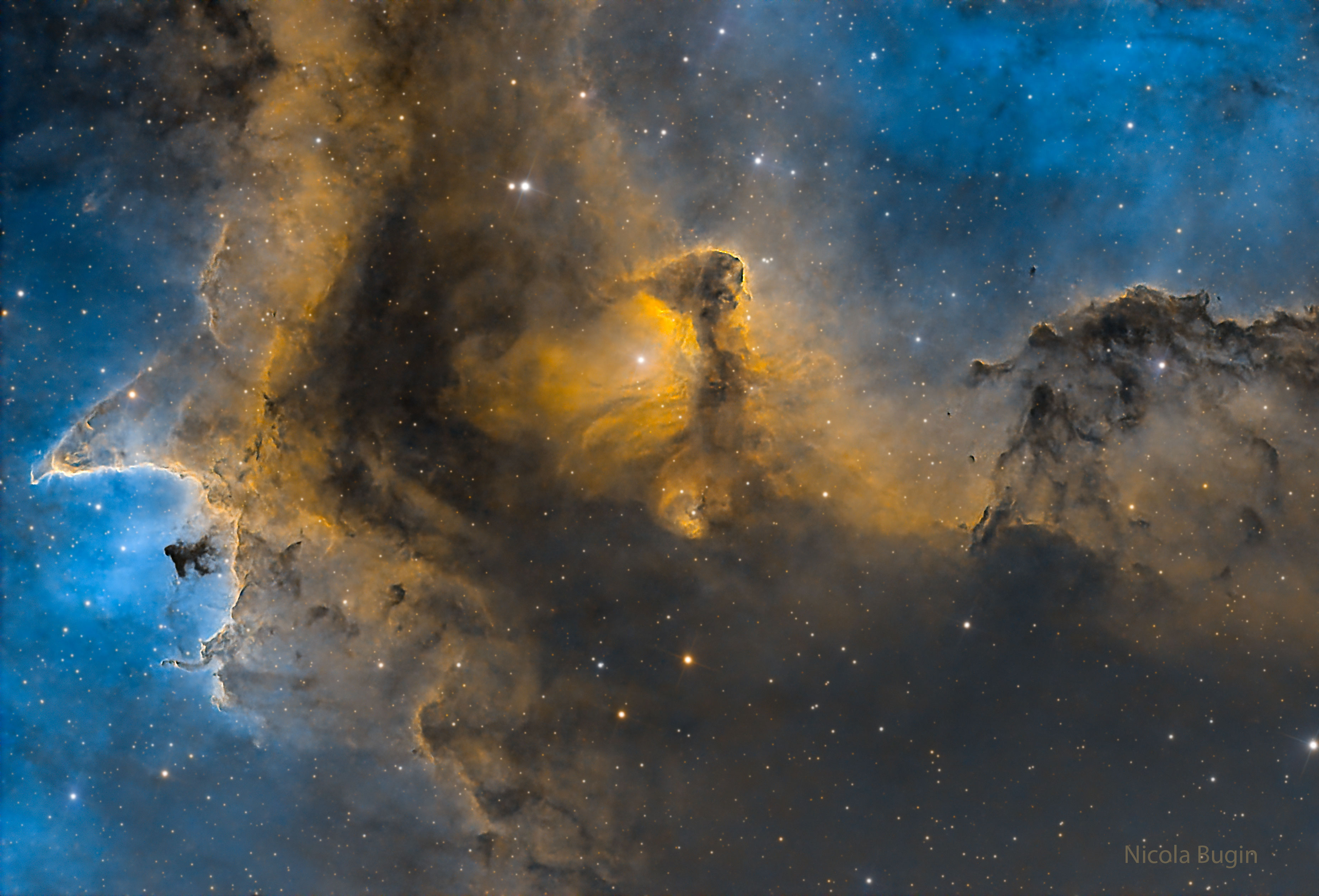 A starfield is shown with a brown and gold tinted dust structures in front of a glowing blue gas background. Please see the explanation for more detailed information.
