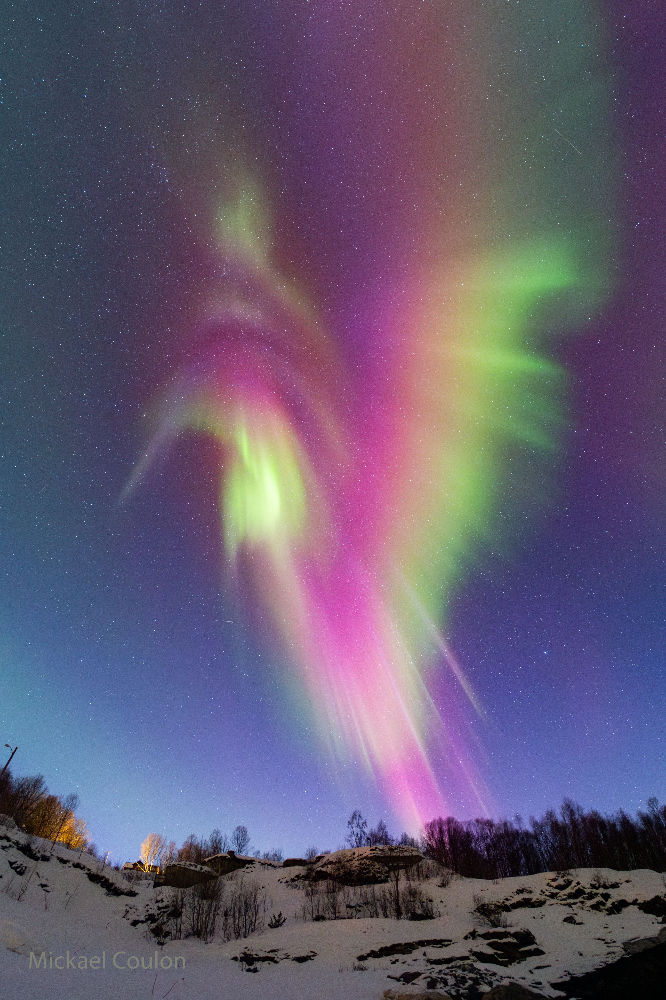 A snowy landscape sits below a star filled sky. Dominating the frame is a large aurora in red, green, yellow, purple, white. Please see the explanation for more detailed information.