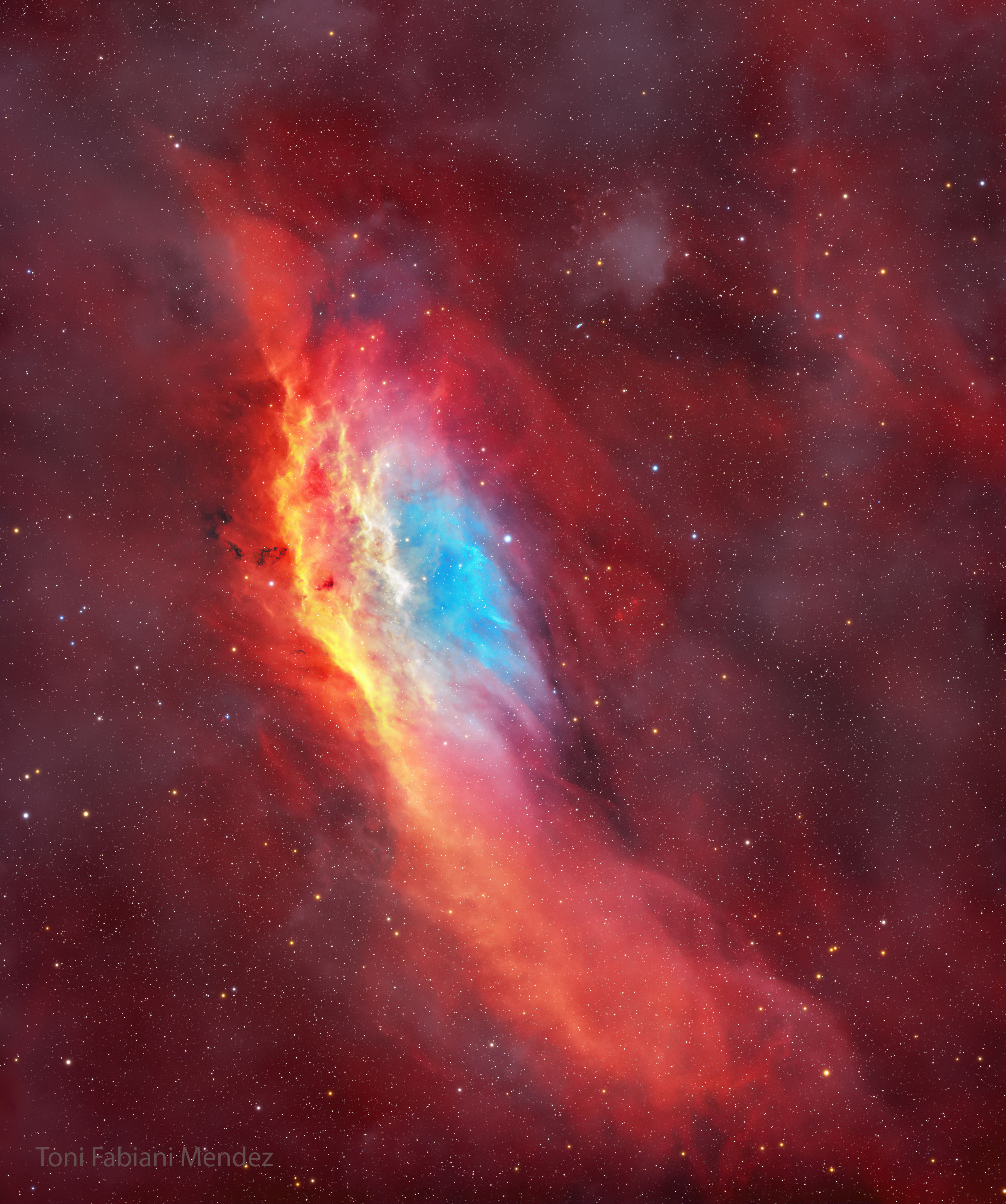 The starry image filled with a red glow features a red, yellow, and blue colored nebula. The nebula has, roughly, the shape of the US state of California. Please see the explanation for more detailed information.