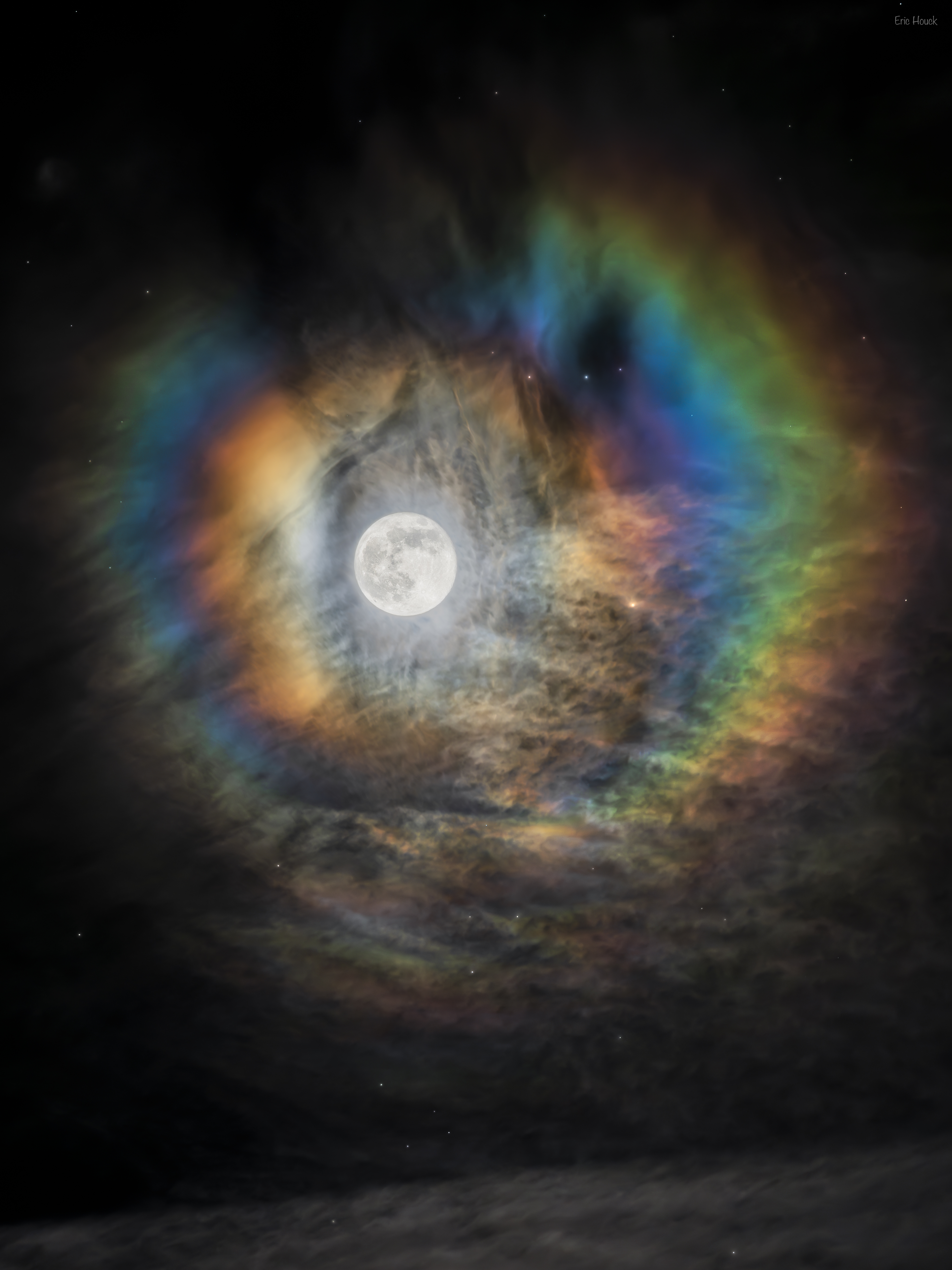The Moon is pictured in the center. ARound the Moon are colorful rings. The rings are nearly circular but have gaps. This but structured clouds are seen around the scene and at the bottom of the frame. Please see the explanation for more detailed information.