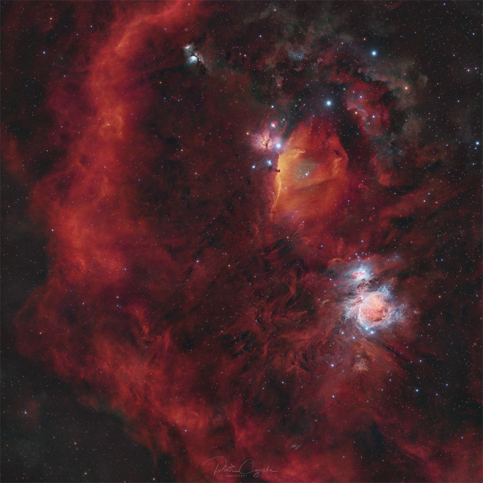 A starfield is shown filled with red glowing gas. On the right is a blue-glowing complex nebula, while on the left there is a long encircling arc of red gas. Please see the explanation for more detailed information.