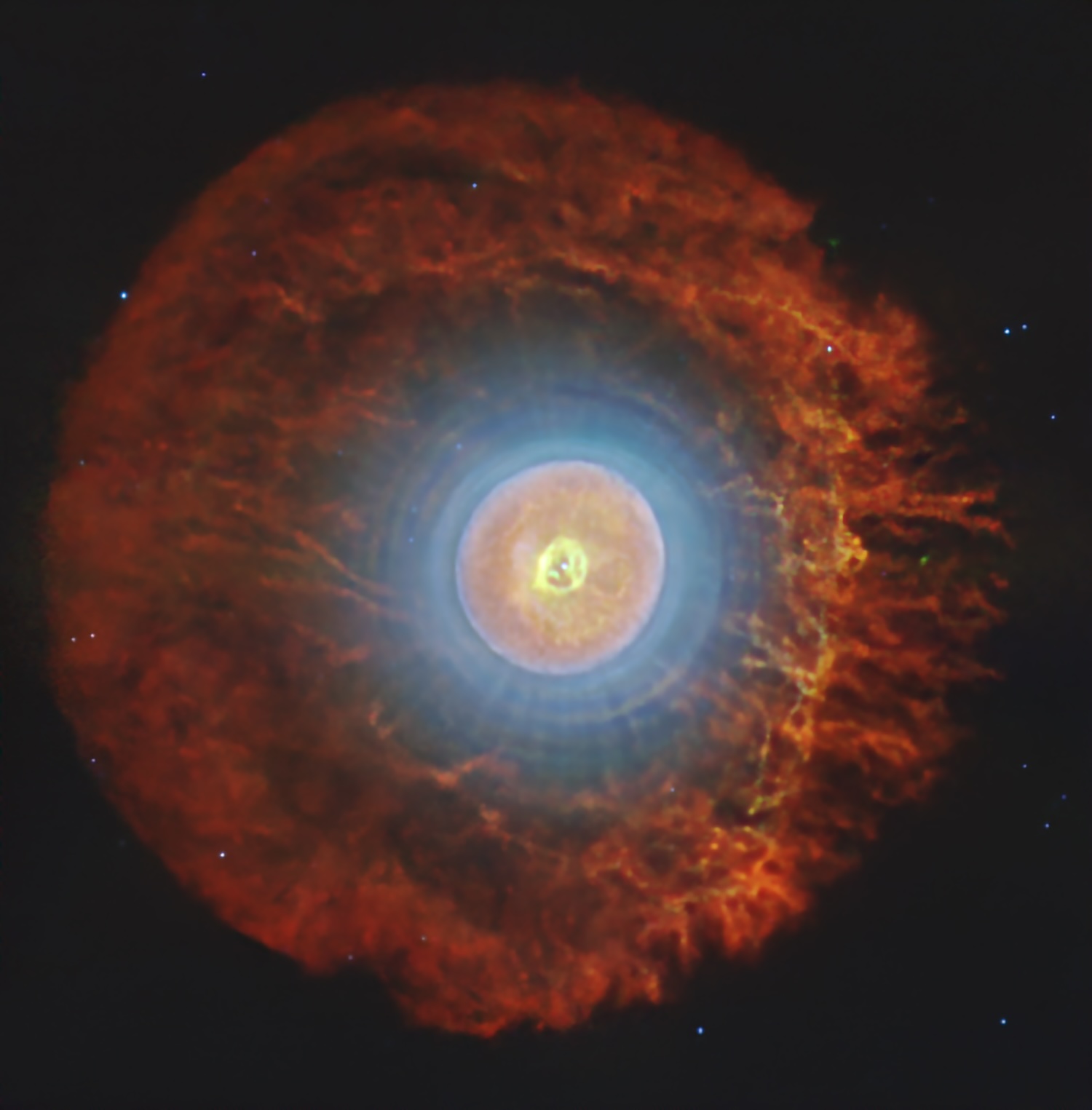 A spherical nebula shows concentric rings of different colors over a dark background with a few stars.