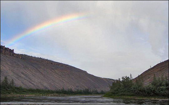Photograph of a rainbow above the Kotuykan River, flanked by steep mountainsides.