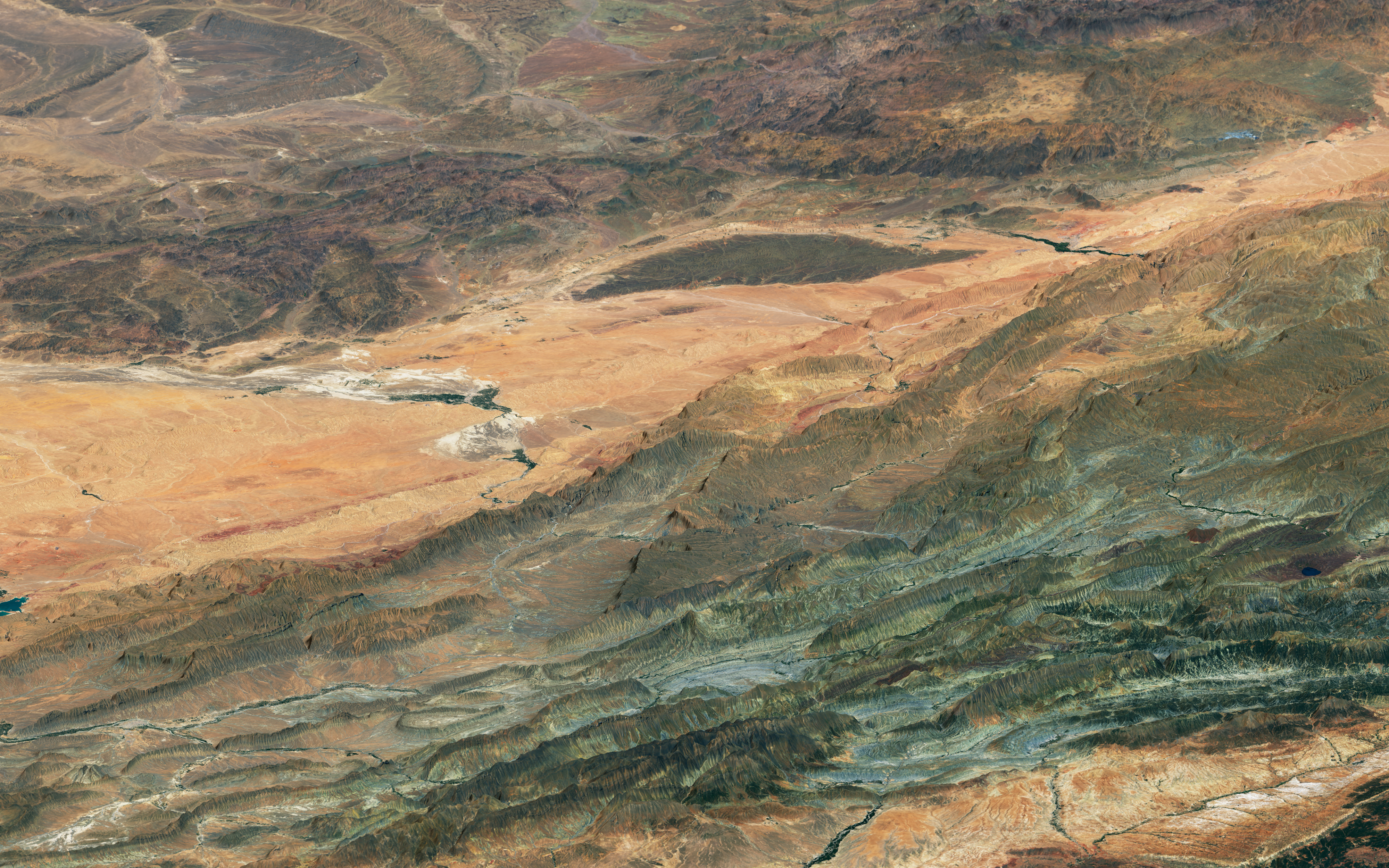 NASA Landsat 8 satellite image of Morocco's High Atlas Mountains showing colorful folded layers of sedimentary rock in purple green white and black ridges across the landscape
