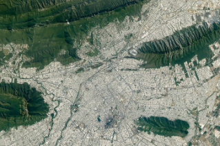 The light-colored urban development of Monterrey, Mexico, fills most of the top half of the photo, and green parallel mountain ridges arc across the bottom of the frame.
