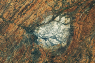 A round, white rock outcrop is surrounded by orange rocks with a north-south linear pattern. Branching riverbeds cut through the rock structures.