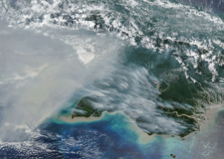 Smoke covers much of the southern third of New Guinea, while clouds and east-west-running mountain ranges are visible in the northern part of the island.