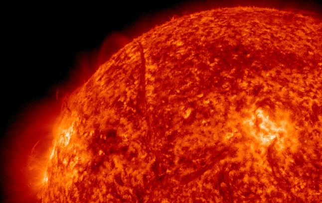 A close-up, animated view of the Sun's surface shows a massive, glowing, swirling eruption of solar plasma. A bright, fiery filament arcs upward from the surface, showcasing the dynamic, intense energy of solar activity.