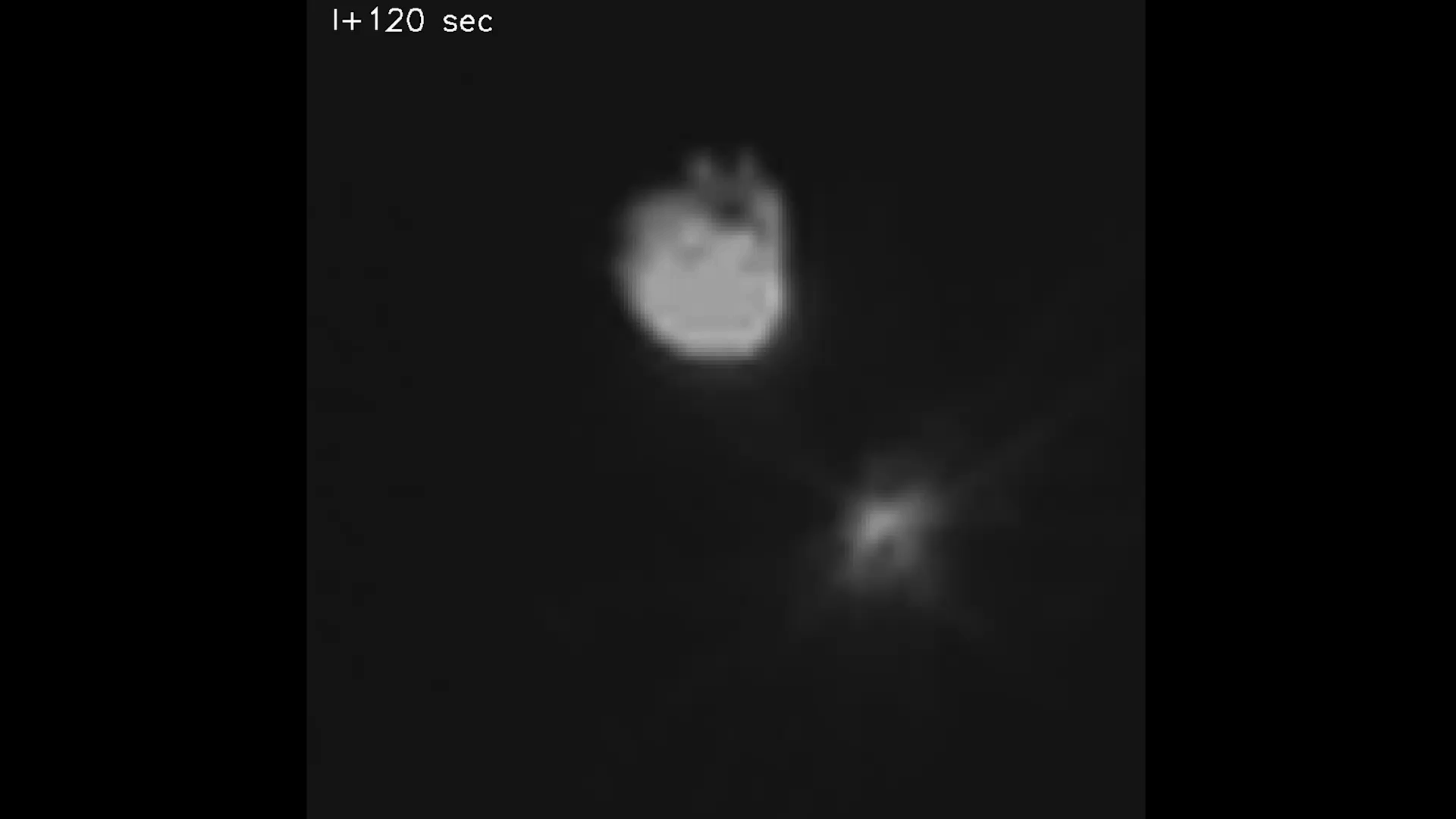 Two gray objects are rotating in synch back and forth, against a black background. The object on top is bulbous and much larger and textured then the object below it. It also is lit up in bright white at the bottom. A smaller bright spot below the large object is unique because extending from it is a cone of streaks or lines that stretch outward into the black background.