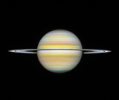 A straight-on view of Saturn, a globe with pale yellow horizontal bands at the equator and orange and pink at the mid-latitudes. Some bands towards the north and south pole have a light blue hue. There are prominent horizontal rings circling at the equator.