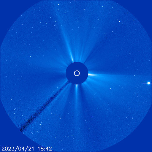 A circular, blue-colored view shows stars around the Sun, which is covered by a dark blue disk at the center. A small white circle in the center of the disk shows the size of the Sun. Streams of material extend away from the disk, and then a white halo of material erupts and moves away from the disk in all directions. A bright dot appears on the right.