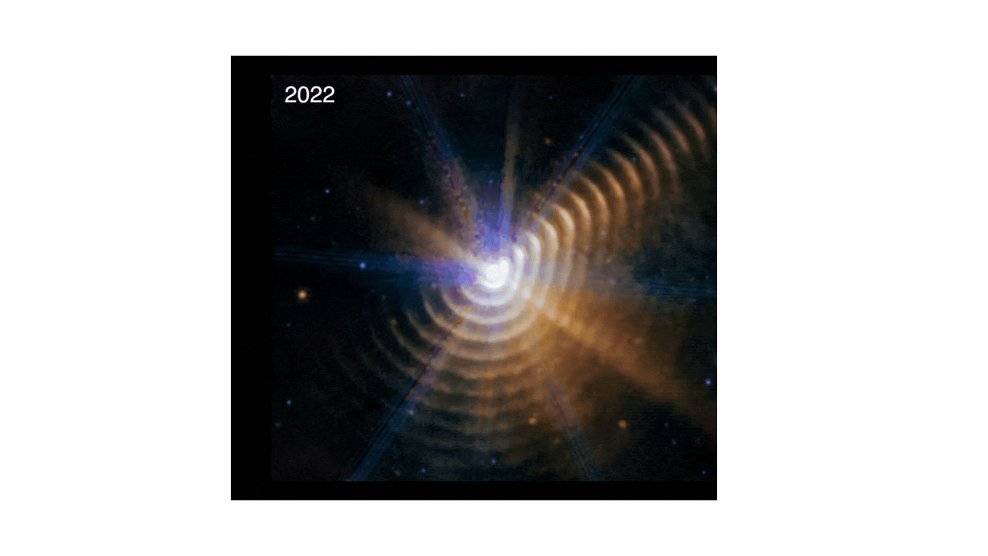The video alternates between two James Webb Space Telescope images of the two-star system Wolf-Rayet 140, the first taken in 2022 and the second in 2023.  Both show a bright white point of light surrounded by 17 regularly spaced, hazy dust shells at the bottom, right, and upper right. There is noticeably less color in the upper left. The central point, where the two stars are located, has a rough hexagon shape.  By alternating between them, it’s clear that the dust shells are moving outward, becoming wider.