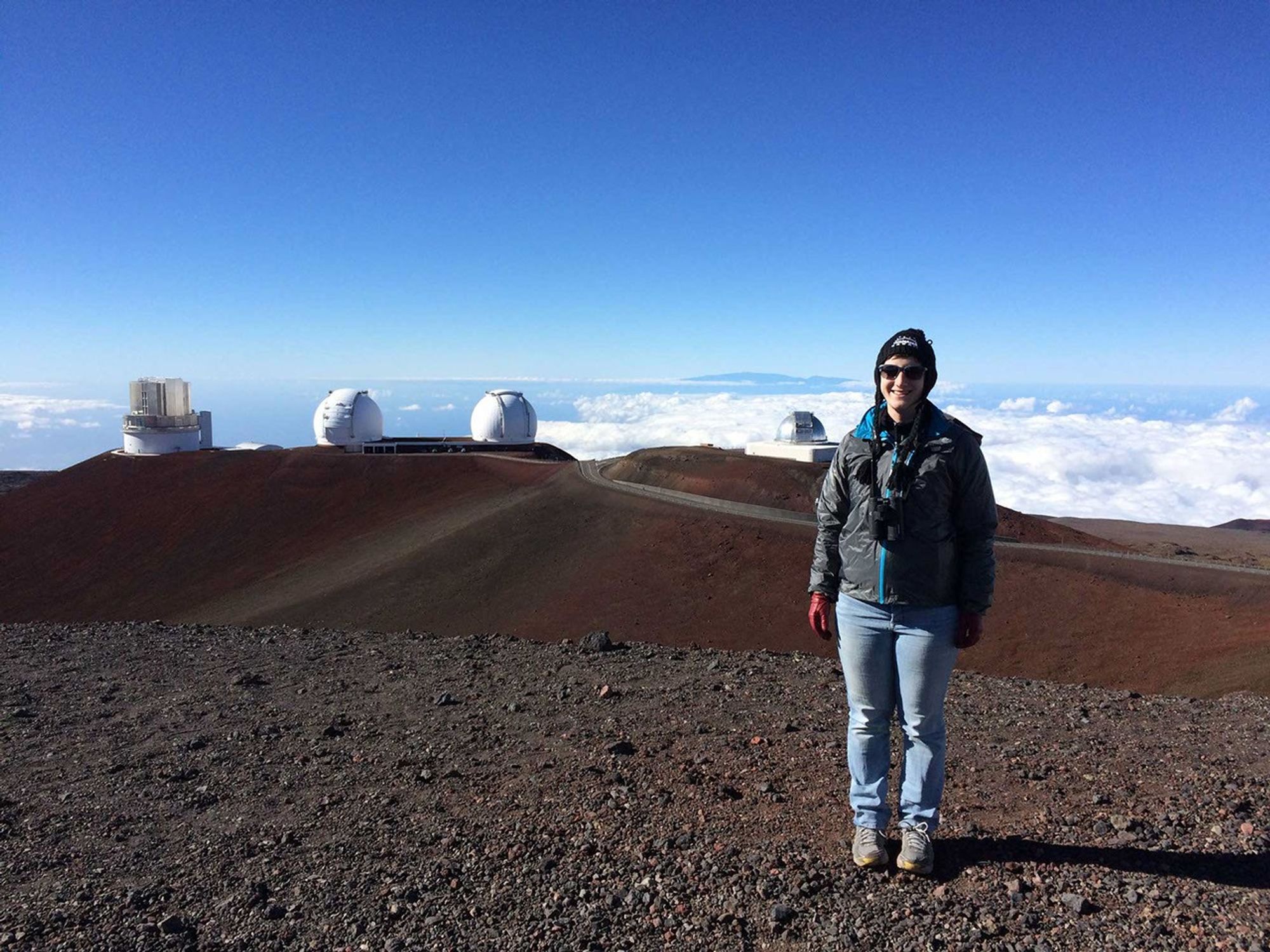 A woman stands in front of three telescope domes in the background.