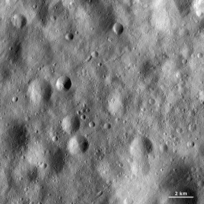 Black-and-white image of the Moon’s cratered surface, showing clusters of small and medium impact craters, with a 2 km scale bar at the bottom.