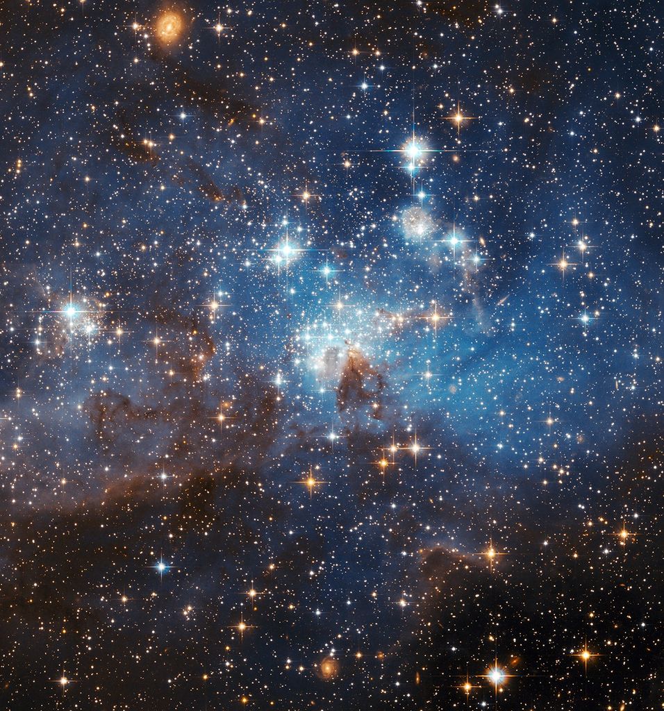 Many glowing stars, some especially bright with small chunks of white dust, with hazy blue gas and clumps of dark red-black dust.