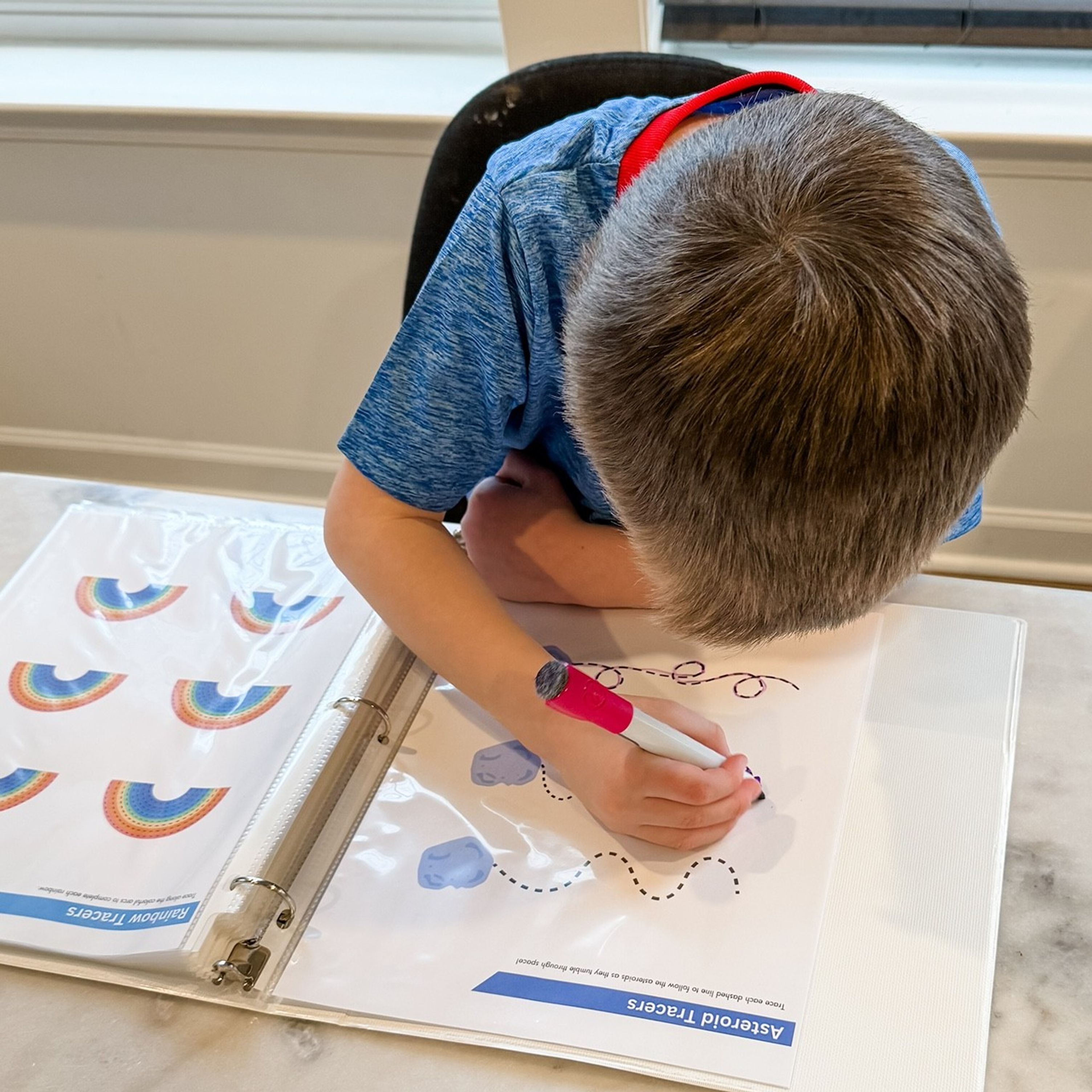Photo showing a boy drawing with a marker on one of the Pre-handwriting tracer sheets.