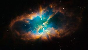 This planetary nebula takes up the entire frame. It is surrounded by an orange oval of wispy clouds shaped almost like lips. Inside the oval is a bright blue cloud pierced by a few small spikes of the orange clouds.