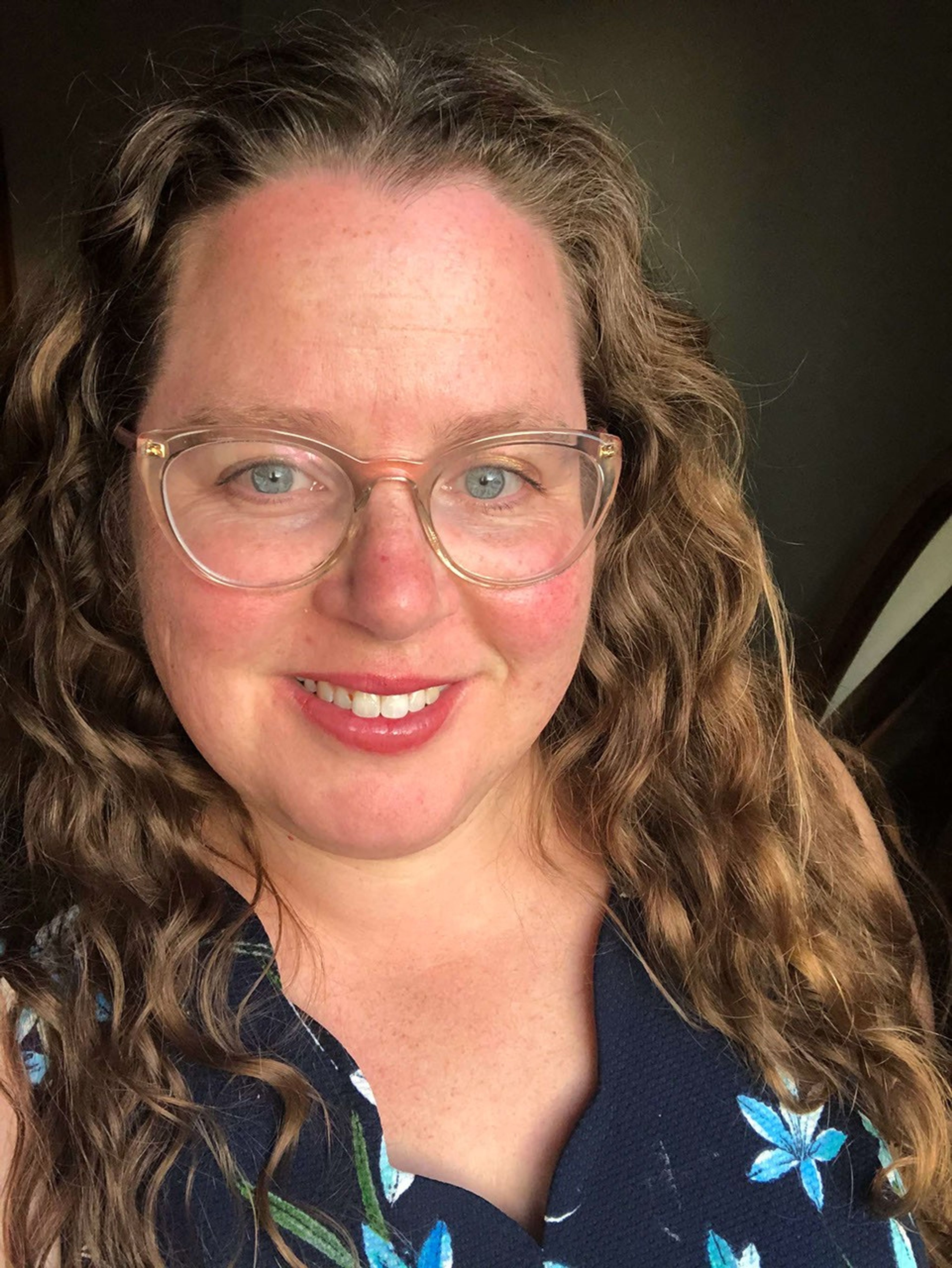 Portrait photo of a smiling woman wearing glasses and with long wavy blonde hair