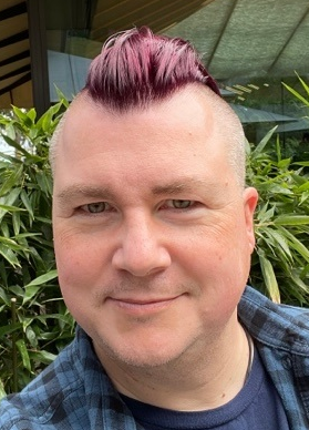Close up image of a white man with brunette and dark red mohawk