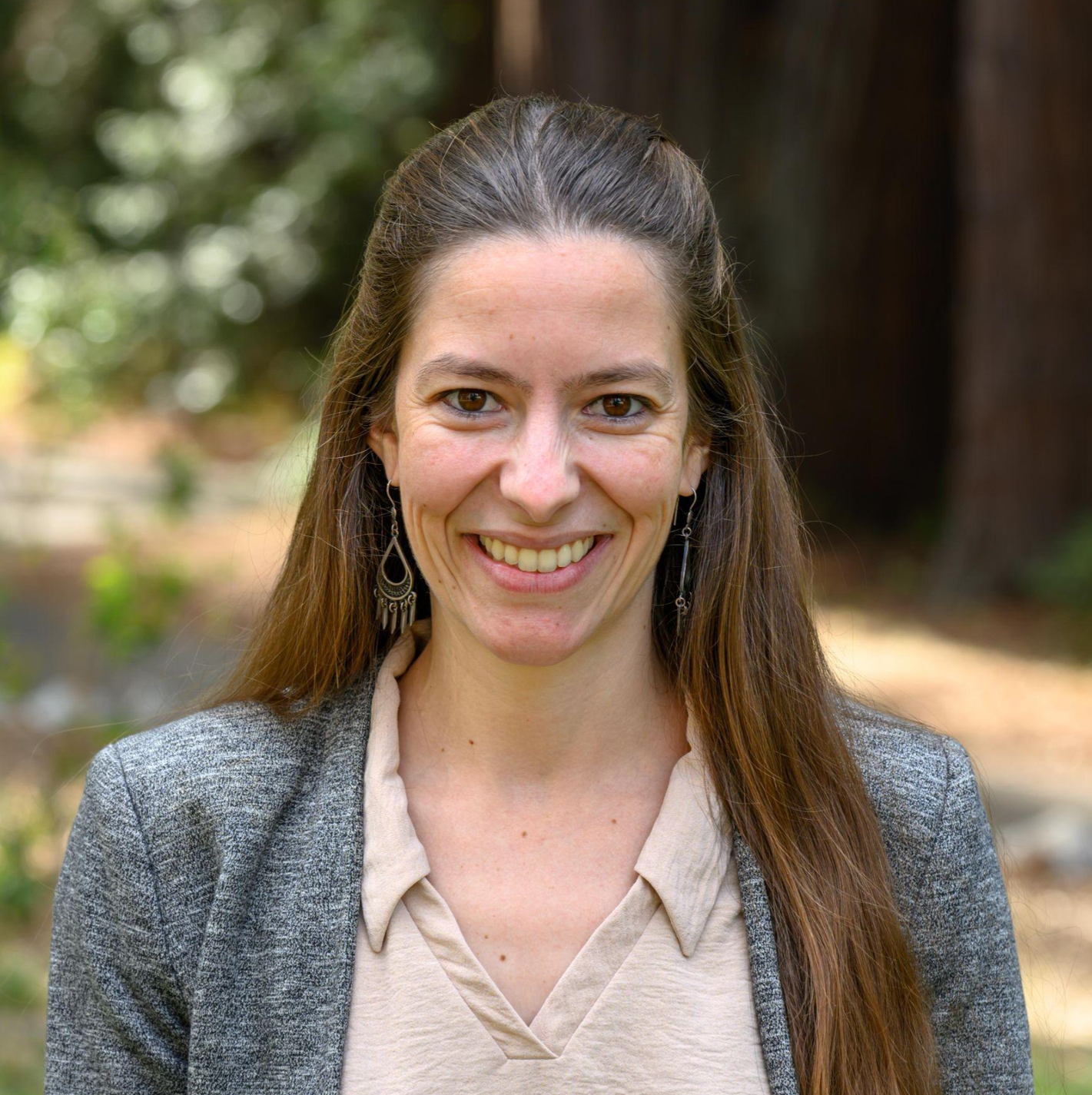 Headshot of Maissa Salama, female, smiling, brown hair, long, parted down the middle, gray blazer, beige button-down plaid shirt.