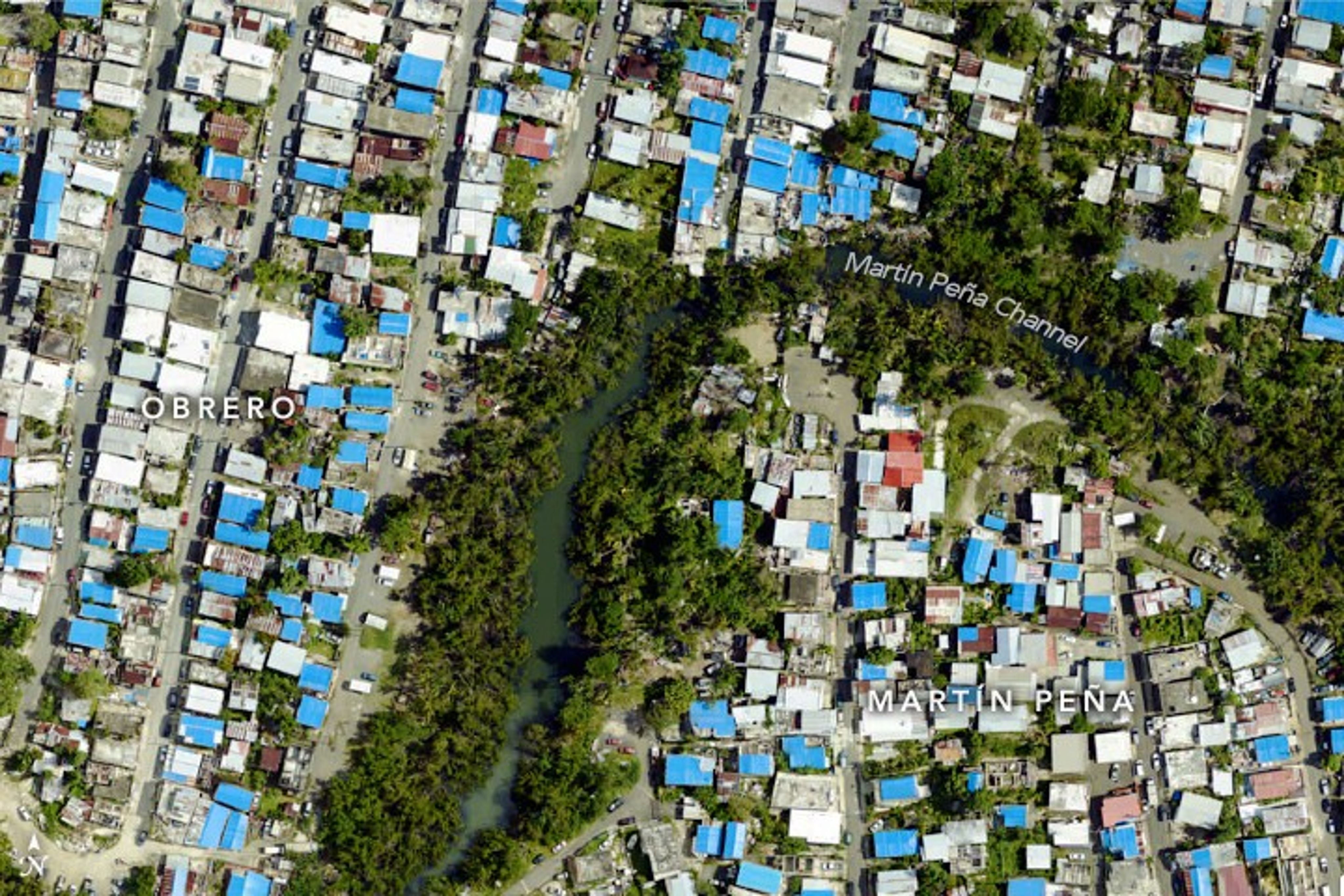 An aerial image that shows homes along a river. Some of the roofs appear blue where the blue tarps are covering damage.