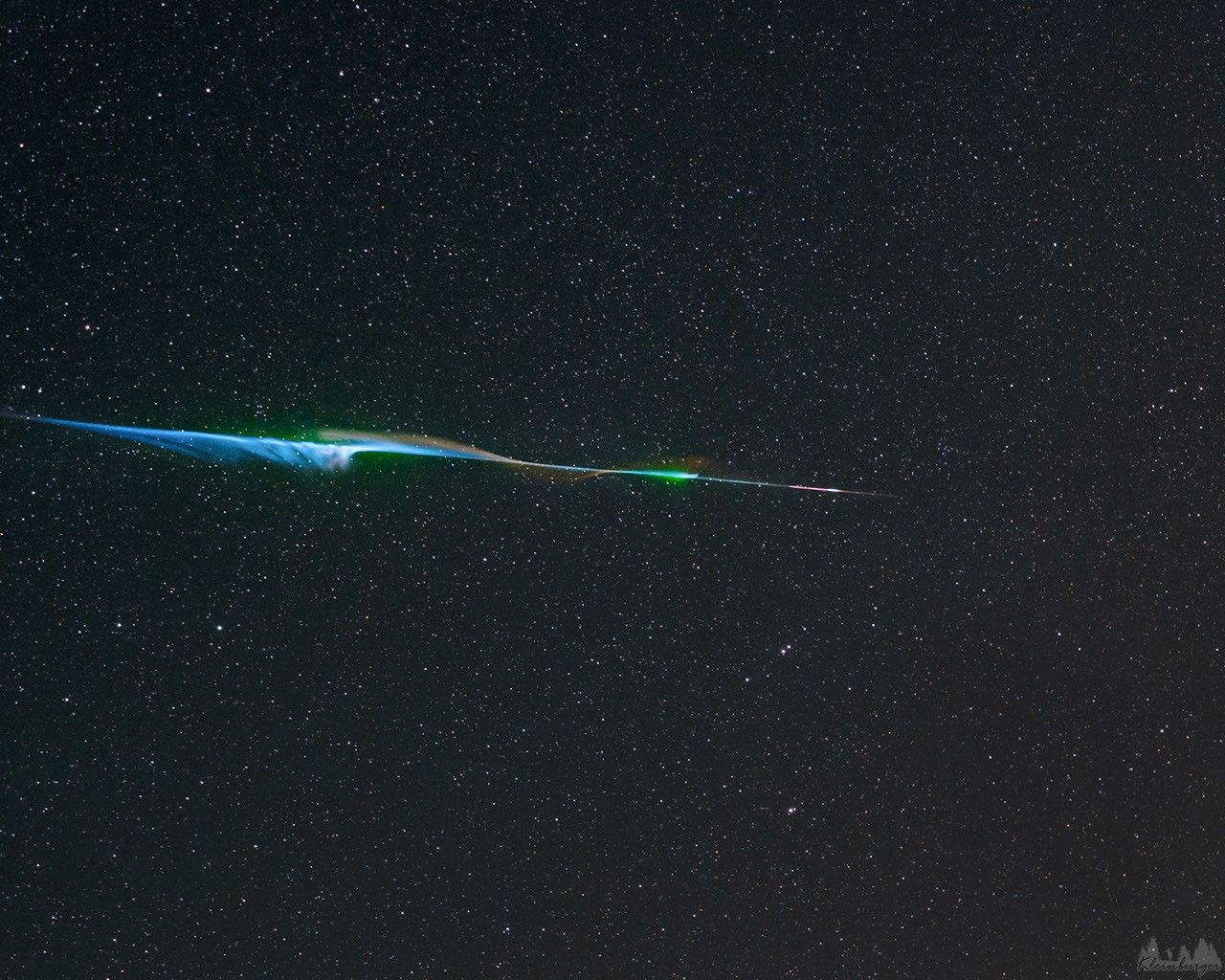 A bright colorful streak crossed the image center, which wisps of colorful gas extending out. In the background is a dark starfield. Please see the explanation for more detailed information.