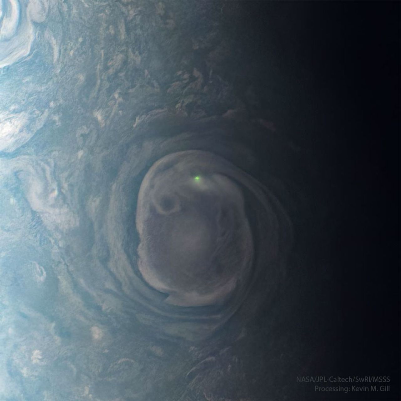 A large swirling cloud on Jupiter is shown with a bright green spot near its top. The cloud is surrounded by other less descript parts of Jupiter's upper atmosphere. Please see the explanation for more detailed information.