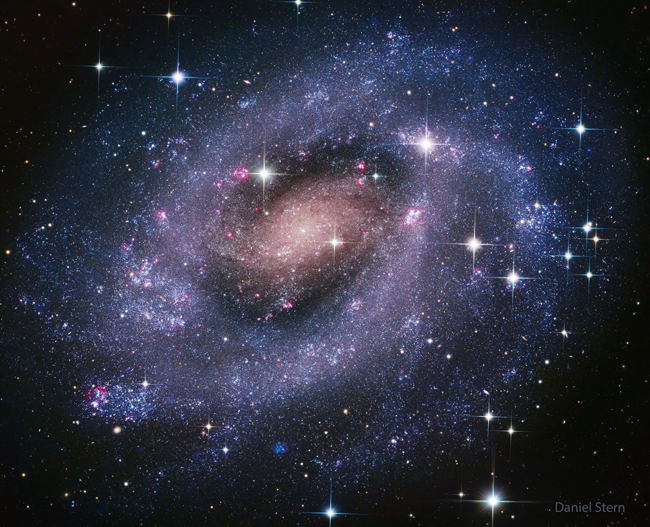 A classic spiral galaxy is shown with blue spiral arms. The center is yellow-red. Many star clusters are easily visible. Please see the explanation for more detailed information.
