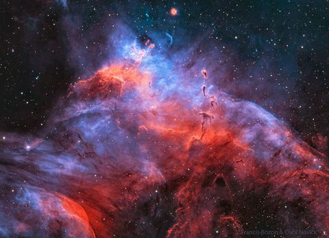 A starfield is shown dominated by a purple and red nebula. Several dark dust pillars are visible that appear not unlike tadpoles. Please see the explanation for more detailed information.