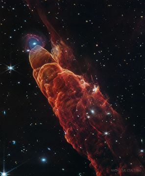 A dark starfield is dominated by a red cone-like nebula with its base on the bottom right and extending diagonally through the image. At the peak of the cone toward the upper left is a background spiral galaxy. Please see the explanation fo