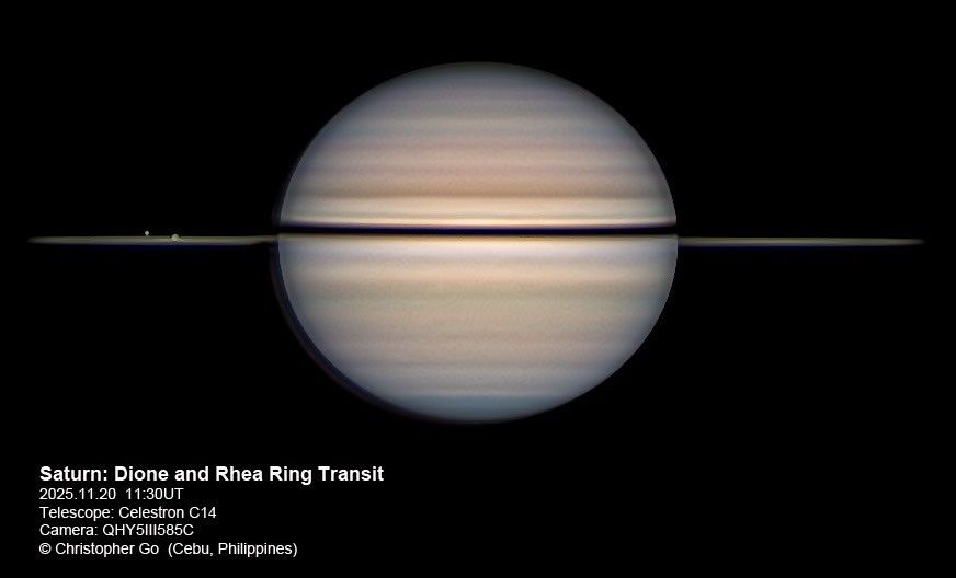 Saturn and its many atmospheric bands occupy the center of the image. Saturn's rings are barely visible as the image is looking along the edge of them. Two small circles, the moons, are traveling across the rings.