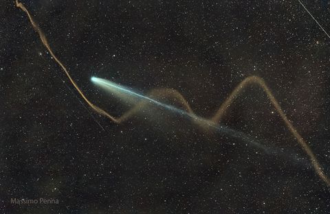 A dark sky shows bright comet with its tails extending diagonally from the lower left. Two tails are visible for the comet -- a long blue tail and a shorter wider white tail. Oddly, a wiggly tan stream appears to be a third tail -- but is a