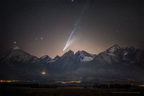 A mountain range is shown in the foreground with a bright comet visible above it. The comet shows tails that are long and bright with the longer tail appearing light blue. Please see the explanation for more detailed information.