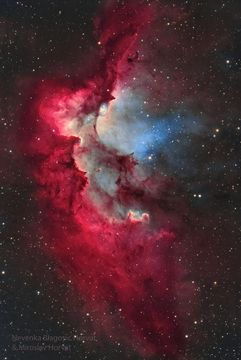 A starfield is shown surrounding a bright gaseous nebula in red with bits of white and blue. Pillars of dust and gas appear around the interior of the nebula pointing to energetic stars in a cluster in the nebula. Please see the explanation