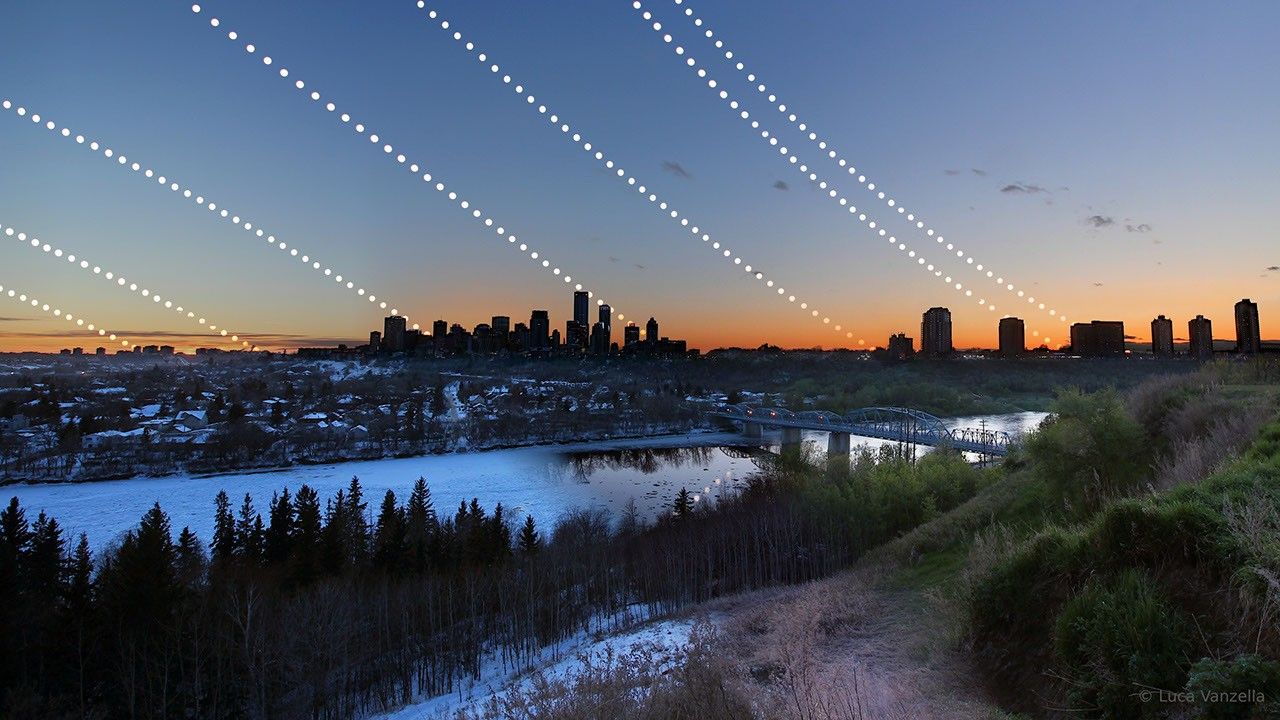 A city skyline is shown behind some hills and a river. The path of the Sun is shown for several times during a year. Please see the explanation for more detailed information.